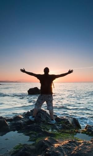 man with arms outstretched over the ocean at sunrise